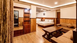 A hotel room with a wooden floor, a bed with white linens, a sofa, a wooden table, and a wardrobe. - Avana Lhayul (Gangtok)