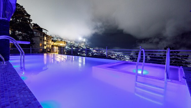 An infinity pool with a city view at night, illuminated by blue lighting. - Avana Lhayul (Gangtok)
