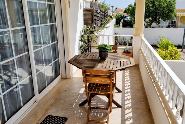 Un balcón con mesa y sillas de madera, plantas en macetas y vistas de los edificios circundantes.