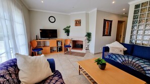 Ein Wohnzimmer mit einer Couch, einem Couchtisch, einem Fernseher, einem Kamin und einer Wanduhr.