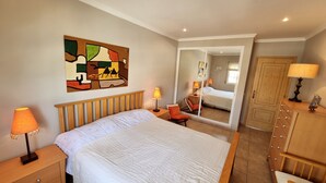 Ein Schlafzimmer mit einem großen Bett, zwei Nachttischen, einer Holzkommode, einem Spiegel und einem farbenfrohen abstrakten Gemälde an der Wand.