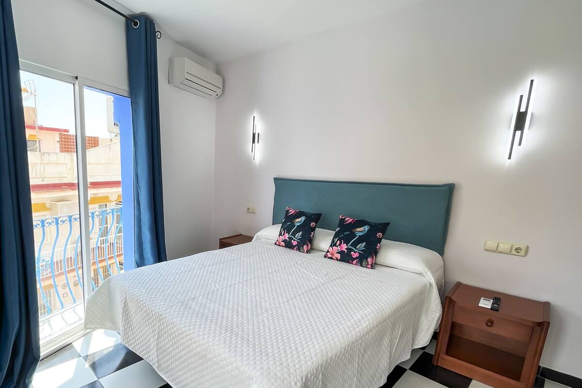 Ein Hotelzimmer mit Bett, Nachttisch, Wand-Klimaanlage und einem Fenster mit blauen Vorhängen.