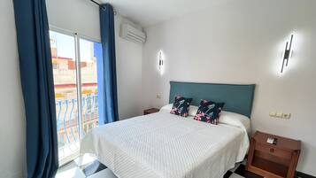 Een hotelkamer met een bed, nachtkastje, wandairconditioner en een raam met blauwe gordijnen.
