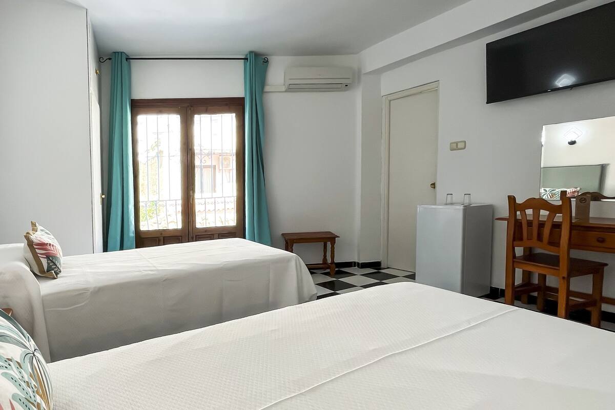 Ein Hotelzimmer mit zwei Betten, einem Schreibtisch, einem Stuhl, einem Fernseher und einem Fenster mit Vorhängen.