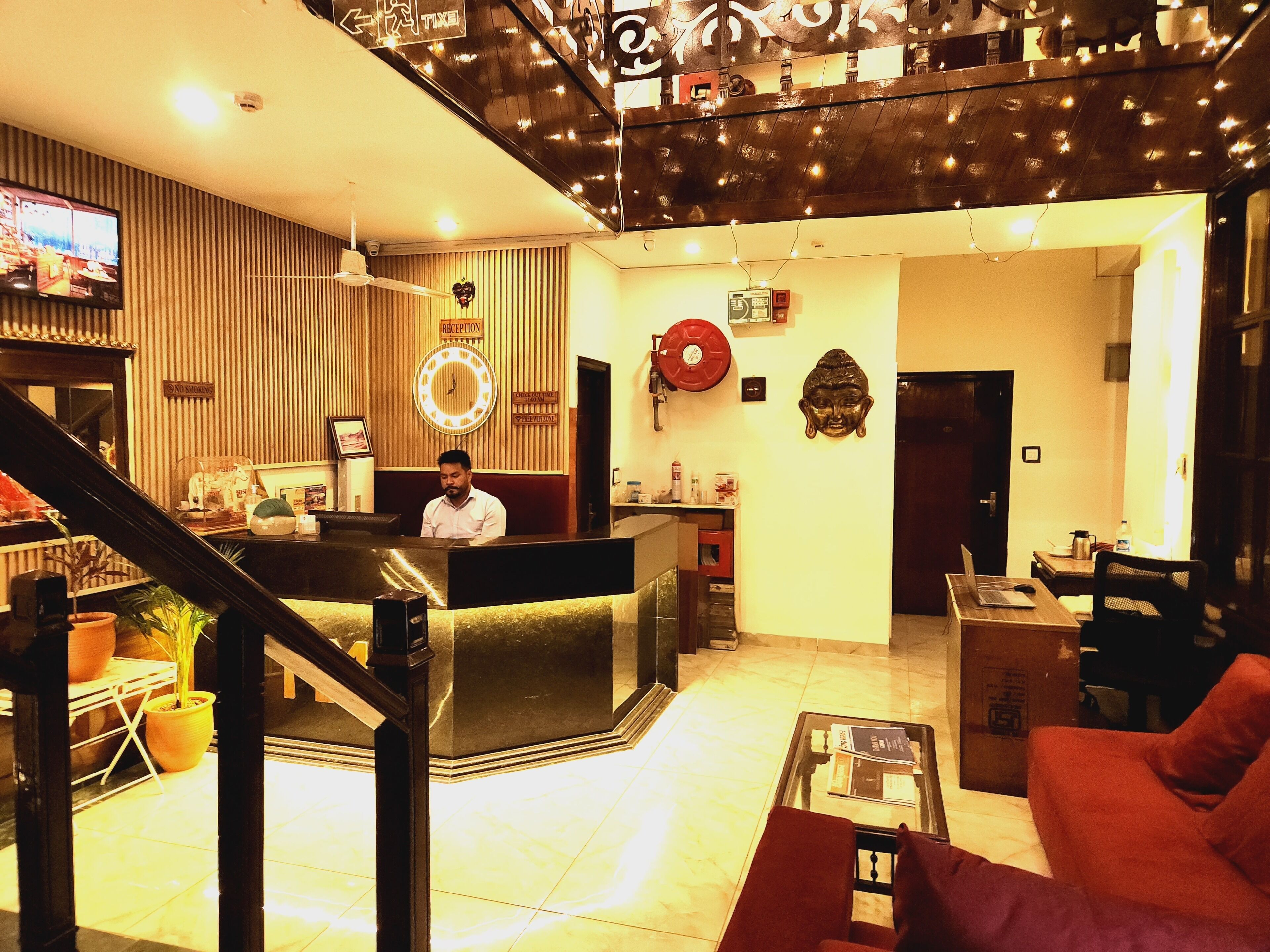 En hotellobby med en receptionsdisk, en klocka, en Buddha-staty och en trappa.