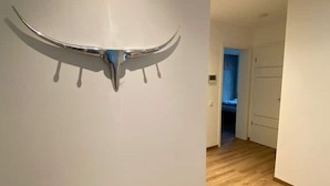 A room with a wooden floor and a white wall with a metallic, curved object mounted on it.