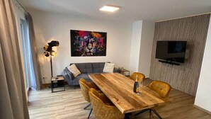 A modern living room with a wooden dining table, two sofas, a floor lamp, and a TV mounted on the wall.