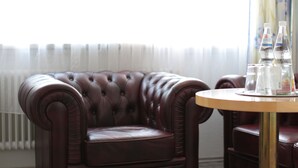 A brown leather armchair with a round wooden table beside it, featuring clear glass bottles and a McDonald's logo. - Boardinghaus zu Coburg (Coburg)
