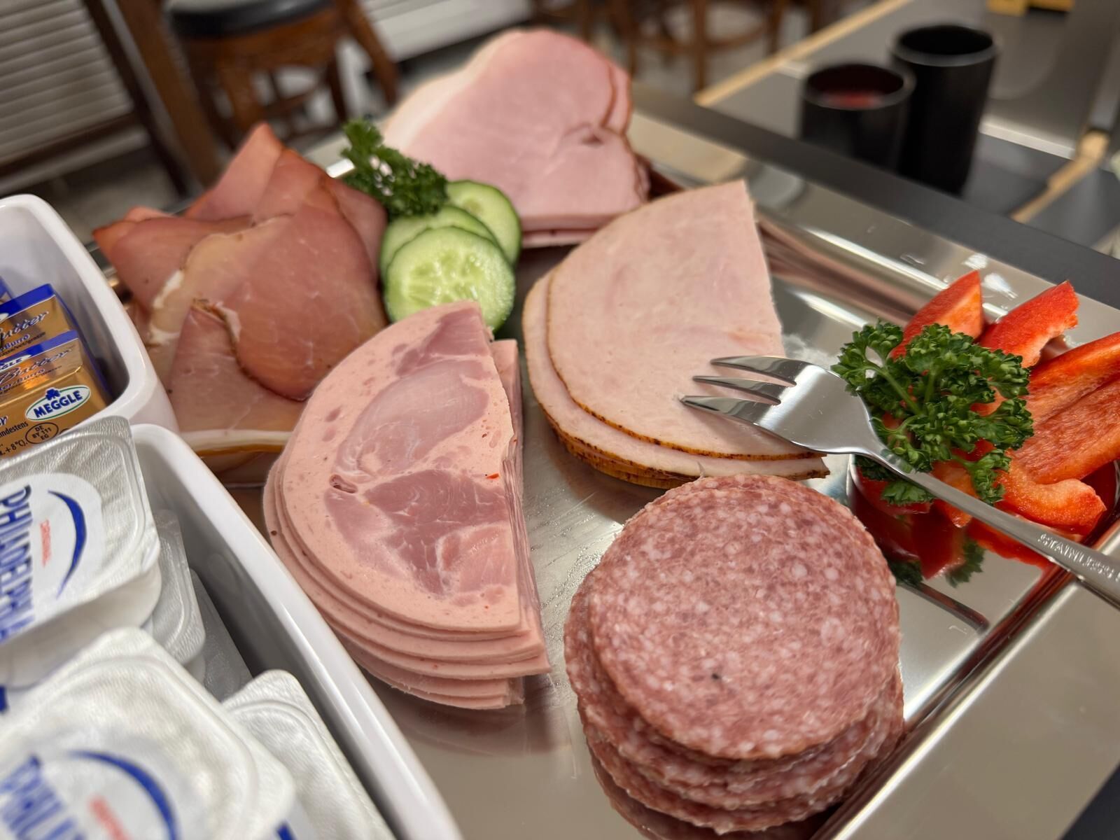 Une table de buffet proposant diverses sortes de viandes, notamment du jambon et du salami en tranches, ainsi que des légumes comme des concombres et des carottes.