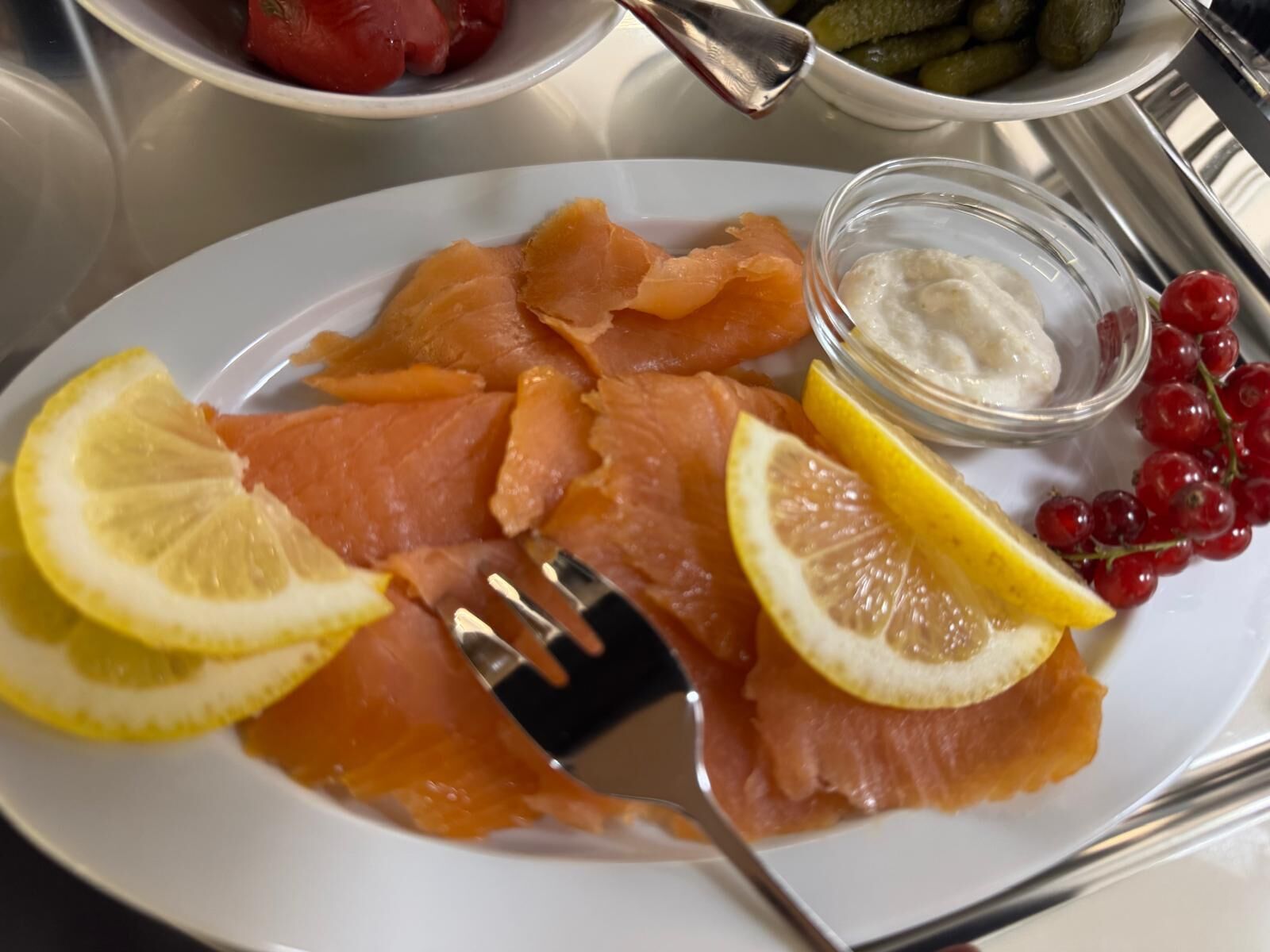 Un plato de salmón ahumado con rodajas de limón y un recipiente pequeño de queso crema.