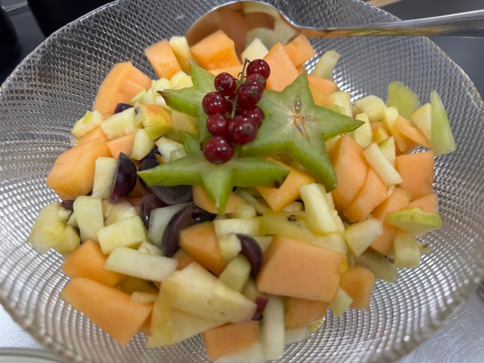 A colander filled with chopped fruits including apples, grapes, and melon.