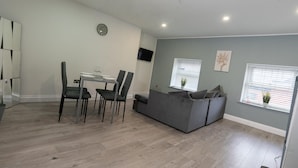 Un salon moderne avec un canapé gris, une table à manger avec des chaises et un téléviseur fixé au mur.