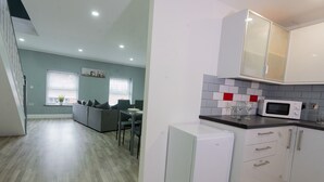 Une cuisine moderne avec des meubles blancs, un four à micro-ondes et un coin repas comprenant un canapé gris et une table.