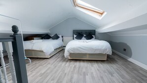 Une chambre avec deux lits, un puits de lumière et un parquet à motifs en chevrons.