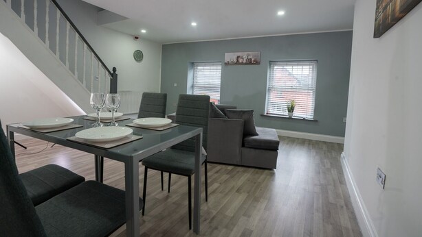 Un salon moderne avec un coin repas, des canapés gris, un escalier et une vue sur la ville grâce à de grandes fenêtres.