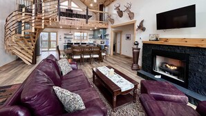 Un salón espacioso con chimenea, una escalera de madera y una cocina al fondo.