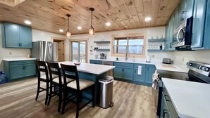 Una cocina moderna con vigas de madera en el techo, armarios azules, una isla central con sillas y un refrigerador de acero inoxidable.