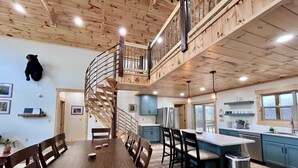Un interior de madera con una escalera espiral, un comedor, una cocina y un oso montado en la pared.