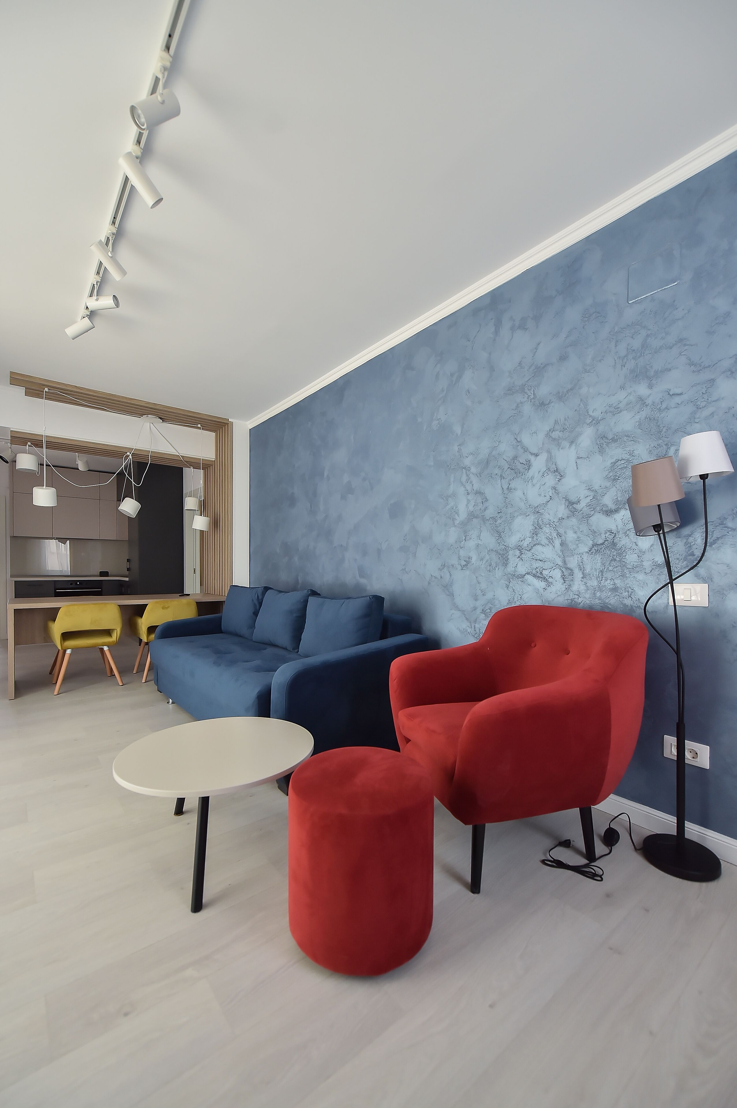 Una sala de estar moderna con una pared azul decorativa, un sillón rojo, un sofá azul y una mesa redonda.