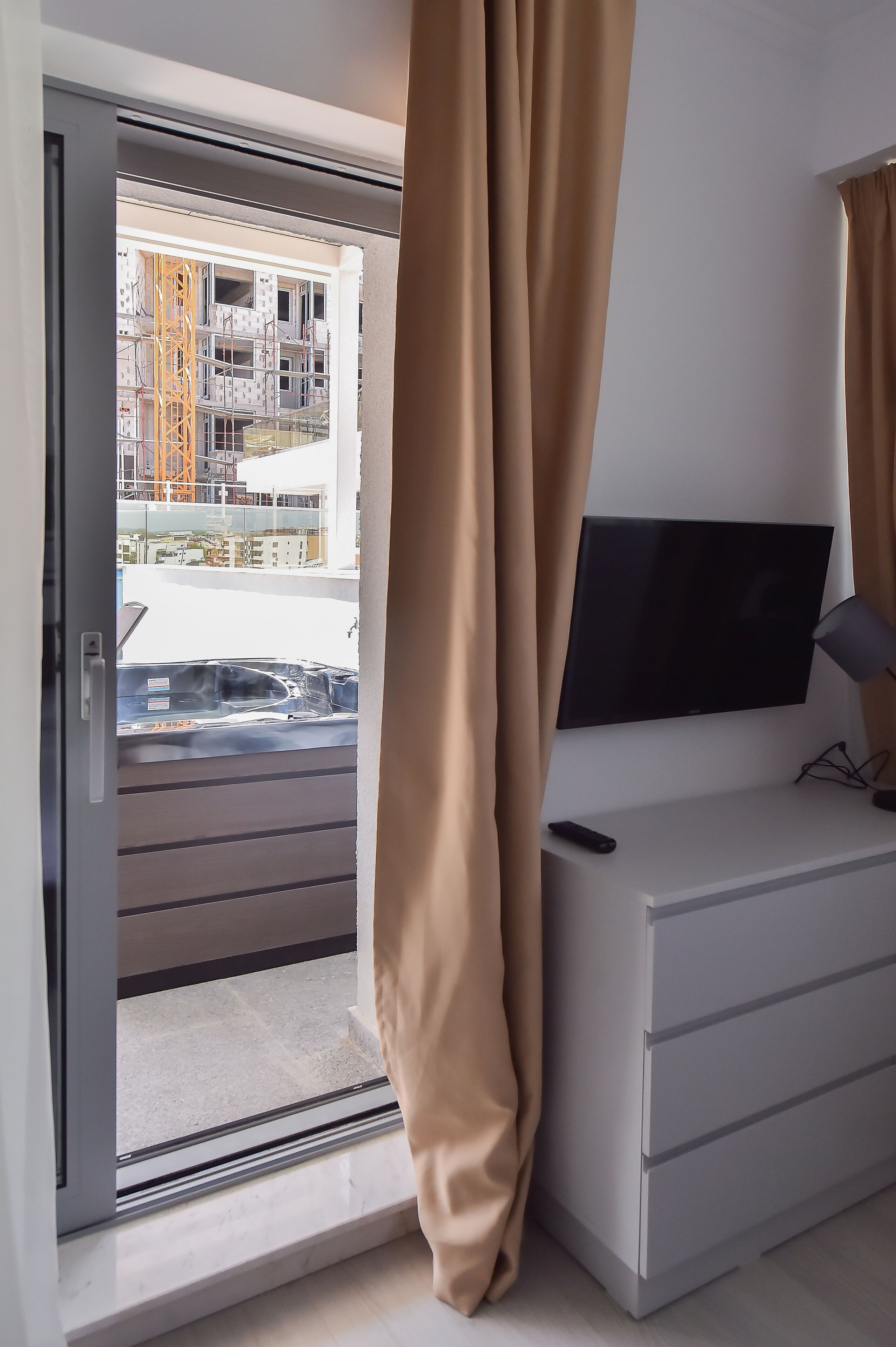 Una habitación con puerta de vidrio corredera que da a un balcón, un televisor de pantalla plana montado en la pared y un aparador blanco.