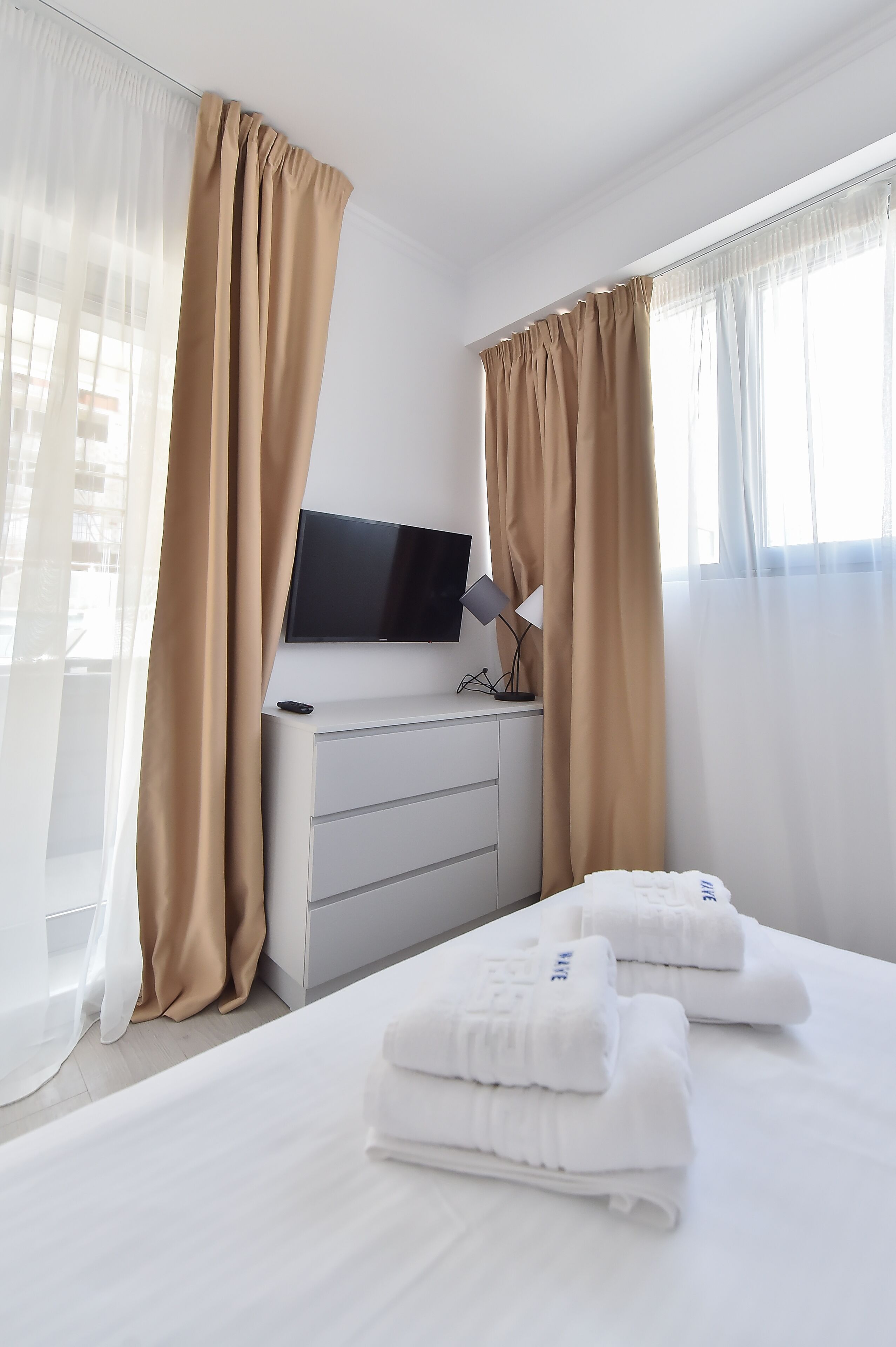 Una habitación de hotel con cama, televisor, escritorio con lámpara y cortinas.
