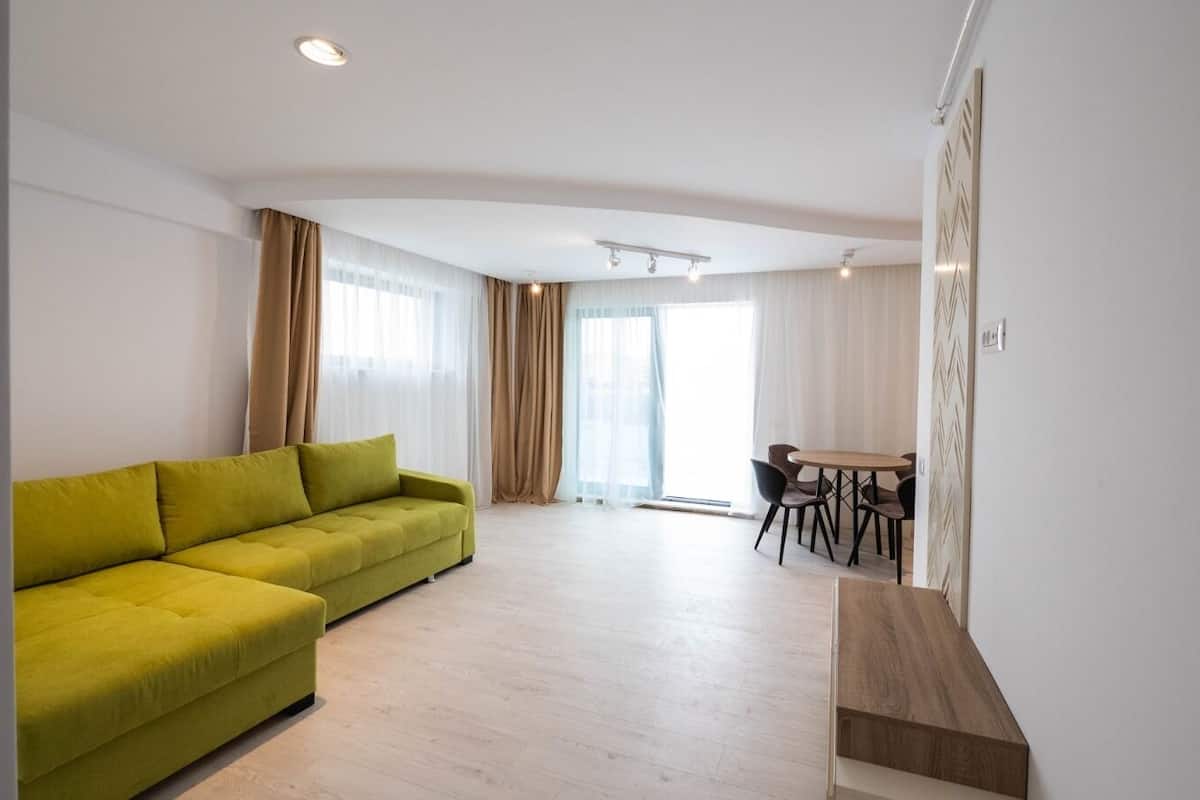 A modern living room with a green sofa, a wooden coffee table, and a dining area with a table and chairs.