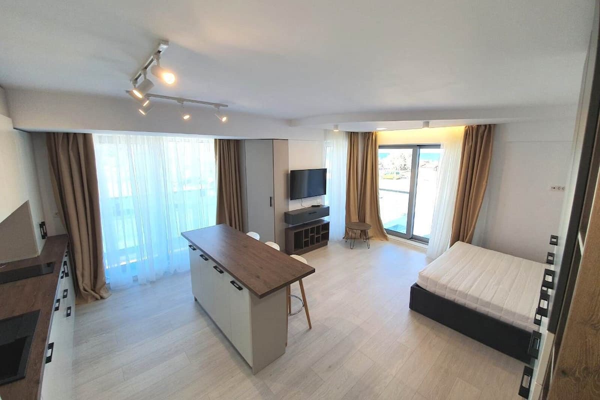 A modern hotel room with a bed, a small desk, a TV, and a balcony with curtains.