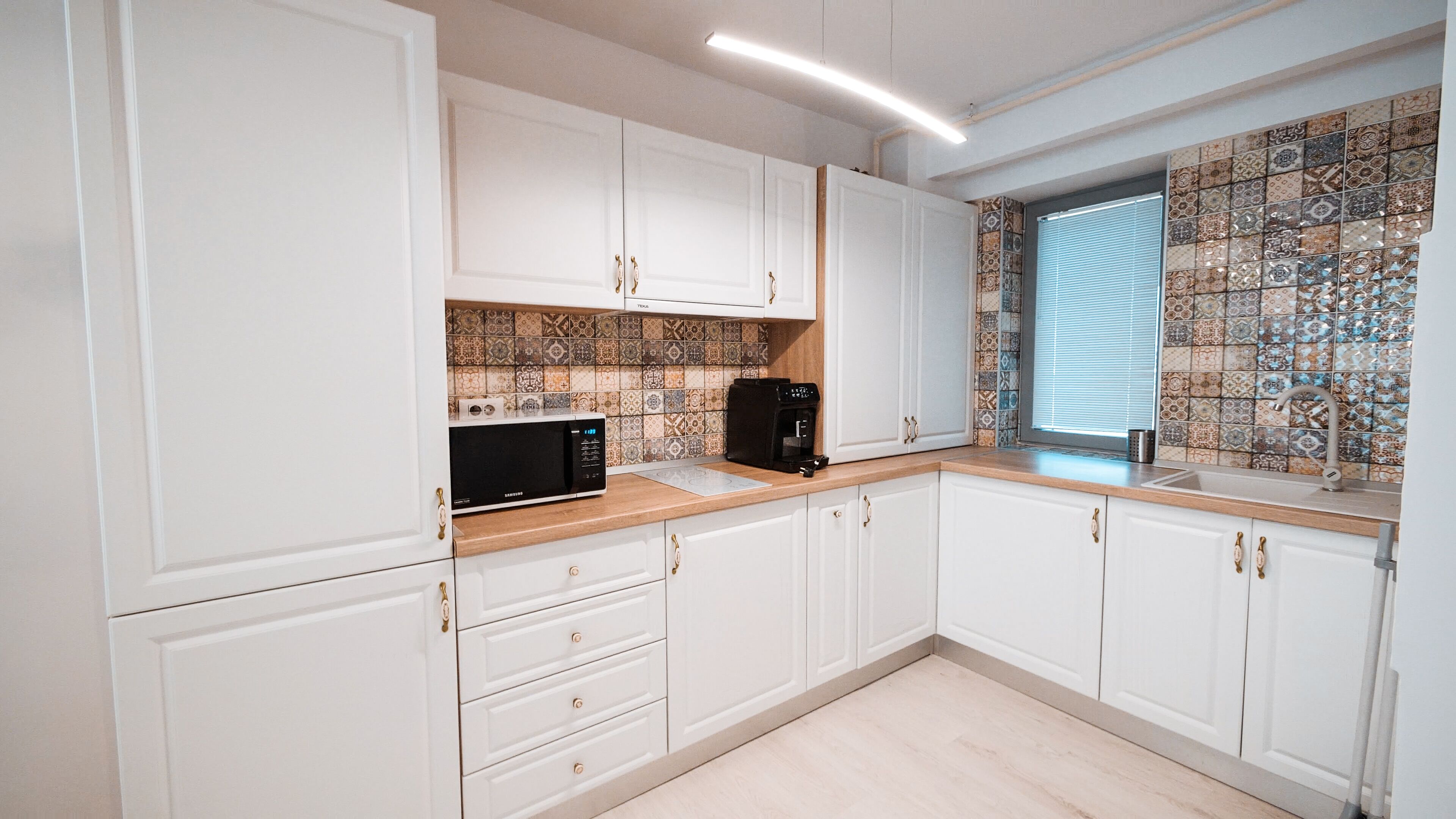 Eine moderne Küche mit weißen Schränken, einer Mikrowelle, einer Kaffeemaschine und einer backsplash-artigen Wandgestaltung.