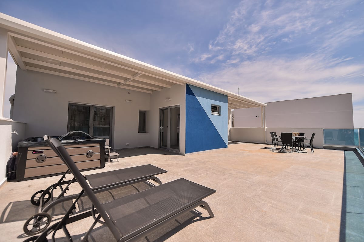 A rooftop terrace with lounge chairs, a hot tub, and a dining area.