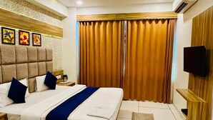 A hotel room with a large bed, a flat-screen TV, a wooden headboard, and a large window with curtains.