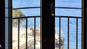 Une vue sur la mer depuis un balcon doté d’une rambarde en corde, d’une porte, et où l’on aperçoit quelques bâtiments au loin.