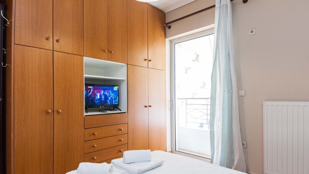 Ein Hotelzimmer mit einem Holzschrank, einem auf einem Regal stehenden Fernseher, einem Bett mit weißer Bettwäsche und Blick durch eine Schiebetür.