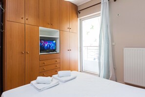 Ein Hotelzimmer mit einem Holzschrank, einem auf einem Regal stehenden Fernseher, einem Bett mit weißer Bettwäsche und Blick durch eine Schiebetür.