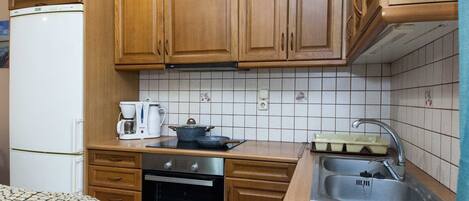 A compact kitchen with wooden cabinets, a built-in oven, a coffee maker, and a sink.