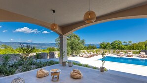Ein überdachter Außenbereich mit Pool, Liegestühlen und Blick auf die Landschaft.