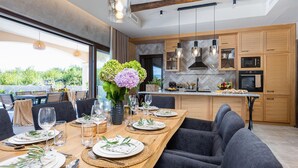 Eine moderne Küche mit Holzausstattung, einer Marmor-Spritzschutzleiste und einem Essbereich mit einem langen Tisch, der für eine Mahlzeit gedeckt ist.