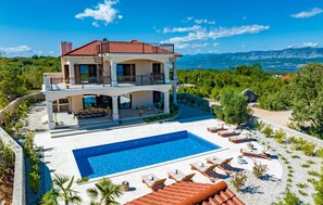 Une maison à deux étages avec une piscine, un espace salon extérieur et une vue sur les montagnes.