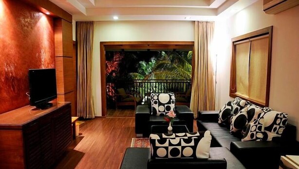Una sala de estar con televisión, sofás de diseño blanco y negro, un aparador de madera y un balcón con cortinas.