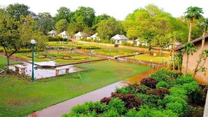 Un jardín con un estanque, senderos peatonales y varias construcciones pequeñas con techos de paja.