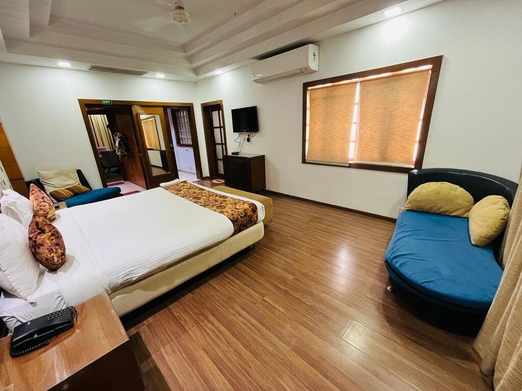 A hotel room with a bed, a sofa, a TV, and a window.