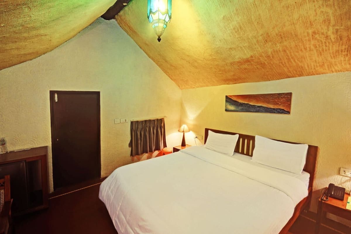 Een slaapkamer met een groot bed, een houten deur, een nachtkastje met een lamp en een schilderij aan de muur.