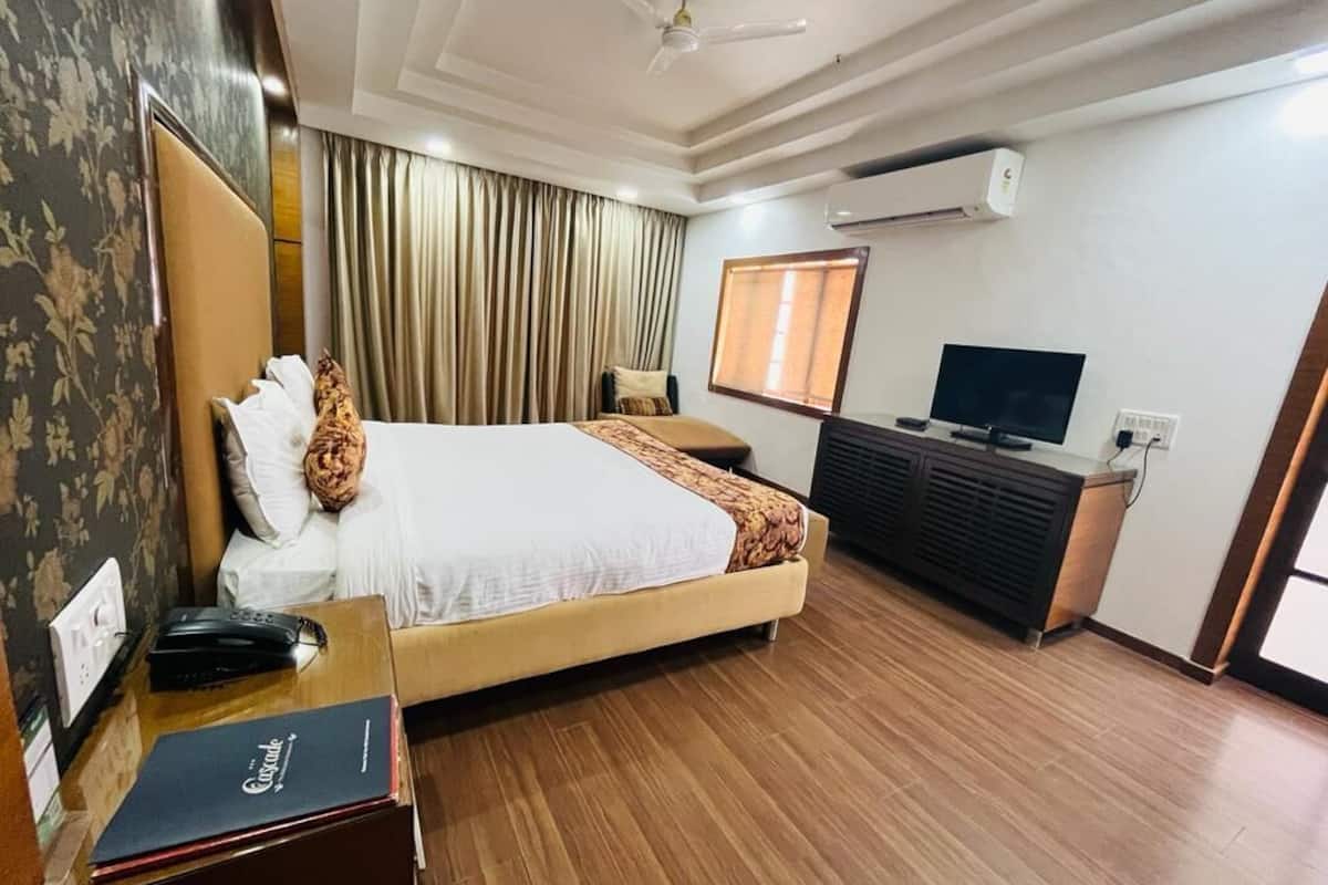 Een hotelkamer met een bed, een bureau met telefoon en boek, een televisie en een airconditioning.