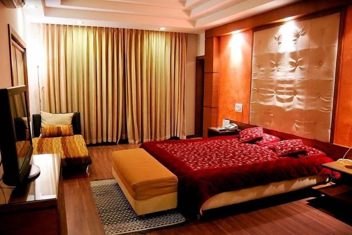Een hotelkamer met een groot bed, nachtkastje, spiegel, televisie en gordijn.
