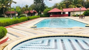 Una piscina con solárium de baldosas, rodeada de vegetación cuidada y palmeras.