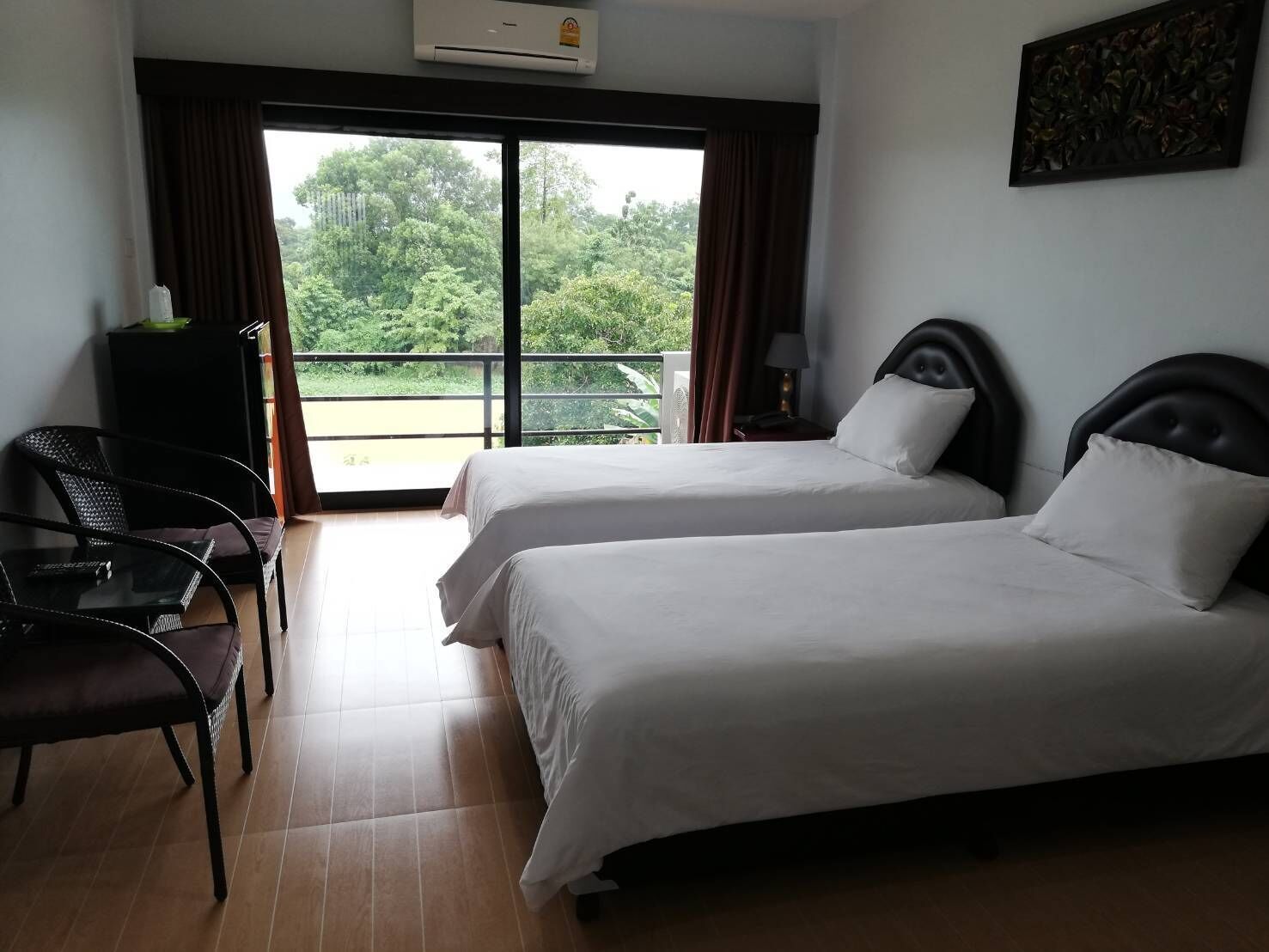 Une chambre d’hôtel avec deux lits, une chaise, une petite table et un balcon donnant sur un paysage verdoyant.