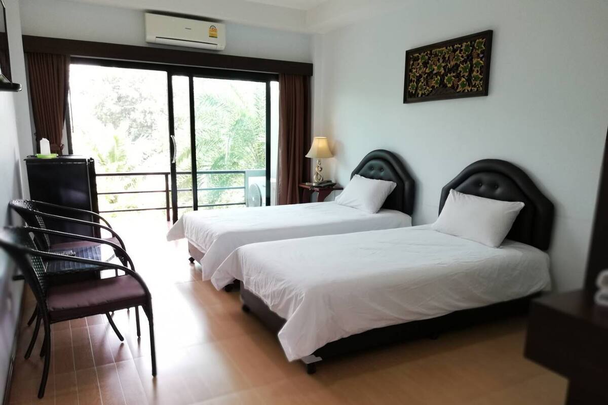 Habitación de hotel con dos camas, un escritorio, una silla y un balcón con cortinas.