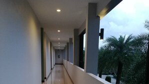 A long, well-lit corridor with a reflective floor, leading to a balcony with a view of palm trees. - Evergreenresort (Makham)