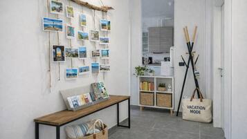 Een gang met een houten bankje, een muur versierd met reisafbeeldingen, een klein boekenrek en een tas met de tekst 'VACATION MODE'.