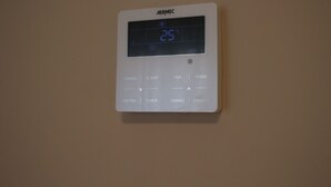 Ein an der Wand befestigtes Thermostat, das 25 Grad Celsius anzeigt.