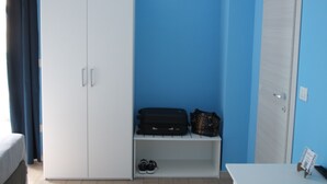 Ein Zimmer mit einem weißen Kleiderschrank, einer blauen Wand, einem kleinen Regal mit Schuhen und Taschen sowie einer Tür.